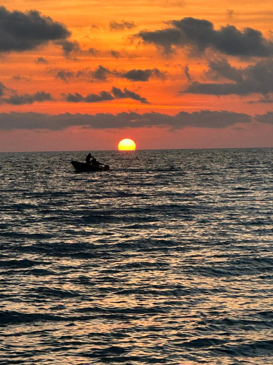 Small boat silhouetted against an orange sunset